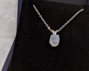 May include: A silver chain necklace with a white oval moonstone pendant. The necklace is displayed in a blue velvet box.