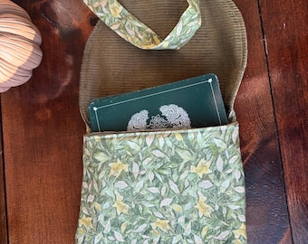 May include: A small, open, green corduroy bag with a floral print pocket and strap. The pocket features a pattern of green leaves and yellow flowers. A deck of cards is visible inside the bag.