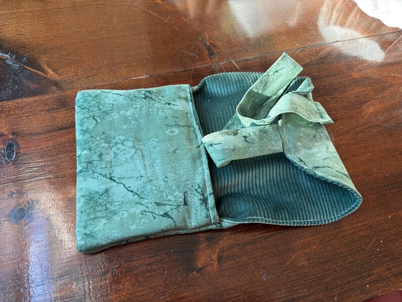 Op de afbeelding: Een teal-kleurige stoffen etui met een gemarmerd patroon op de buitenklep en een corduroy-achtige textuur aan de binnenkant. De etui is open, waardoor de binnenkant zichtbaar is, en heeft een stoffen striksluiting.