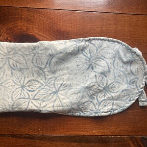 May include: A light blue fabric item with a floral pattern. The fabric is a light blue and white color, with a repeating pattern of stylized leaves. The item is tied with two fabric straps.