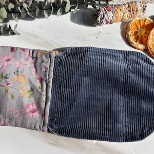May include: A grey and floral fabric pouch with a dark blue corduroy flap. The pouch has a drawstring closure and a long cord tie.