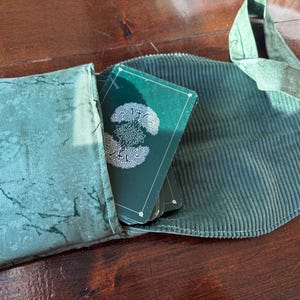 Op de afbeelding: Een groene tarotkaartenset met een wit Keltisch knoopontwerp is gedeeltelijk zichtbaar in een bijpassend groene corduroy etui. De etui is open en onthult de kaarten en een groene kaarthouder van gemarmerde stof.