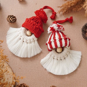 May include: Two white yarn gnome ornaments with red and white striped and solid red knit hats. The ornaments have wooden beads for noses and white yarn beards.