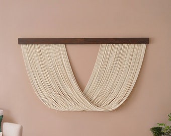 May include: A beige armchair with a green pillow sits in front of a wall with a macrame wall hanging. The wall is painted a light pink color. There are two small tables with gold and black metal legs.