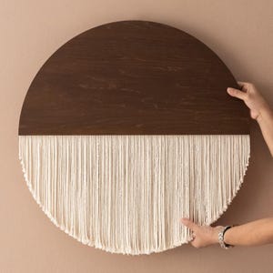 May include: A half-circle wall hanging with a dark brown wooden top and a fringe of white yarn.