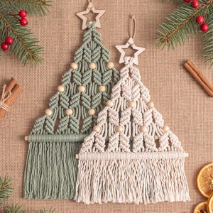 Può includere: Due decorazioni da parete in macramè a forma di albero di Natale, una verde salvia e una color crema. Ognuna presenta una stella in legno sulla sommità, perline in legno naturale intrecciate nel cordoncino e frange con un bastoncino in legno.
