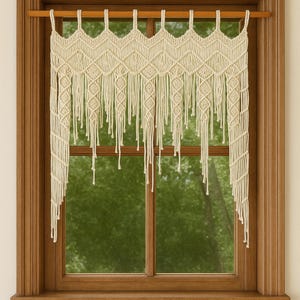 以下が含まれることがあります： クリーム色のマクラメ窓カーテン。カーテンは、長いフリンジが付いた幾何学的なダイヤモンド模様が特徴です。木製の窓枠内の木製のロッドから吊り下げられています。背景には、緑の木々のぼやけた景色が映っています。