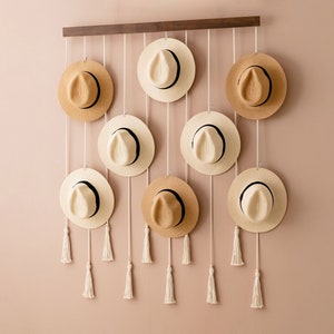 Puede incluir: Un perchero de pared con ocho sombreros de paja colgados. Los sombreros son de diferentes colores y tienen bandas negras alrededor. El perchero es de madera y tiene un acabado marrón oscuro.