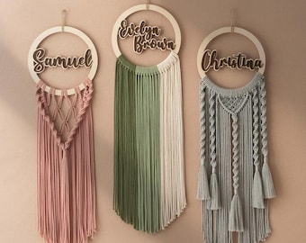 May include: Three macrame wall hangings with wooden hoops and personalised names. The names are Evelyn Brown, Samuel, and Christina. The hangings are in shades of green, pink, and grey.