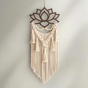 以下が含まれることがあります： 上部に茶色の蓮の花のデザイン、下部にクリーム色のマクラメデザインが施された壁掛け。 マクラメにはタッセルと木製のビーズが含まれており、ボヘミアンな美しさを生み出しています。 薄い紐で吊り下げられています。