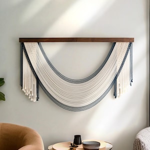 May include: A white and navy blue macrame wall hanging with a wooden dowel at the top. The macrame is in the shape of a crescent moon.