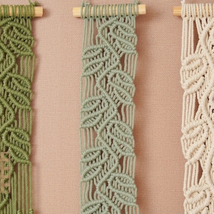 May include: Three macrame wall hangings with a leaf pattern. The hangings are made with natural cotton cord and are in shades of green and cream.