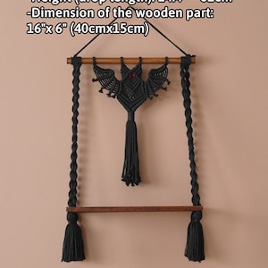 May include: Black macrame bat wall hanging with a wooden shelf and tassels. The bat is 16 inches by 6 inches (40 cm by 15 cm). The hanging is 24.4 inches to 62 cm in length.