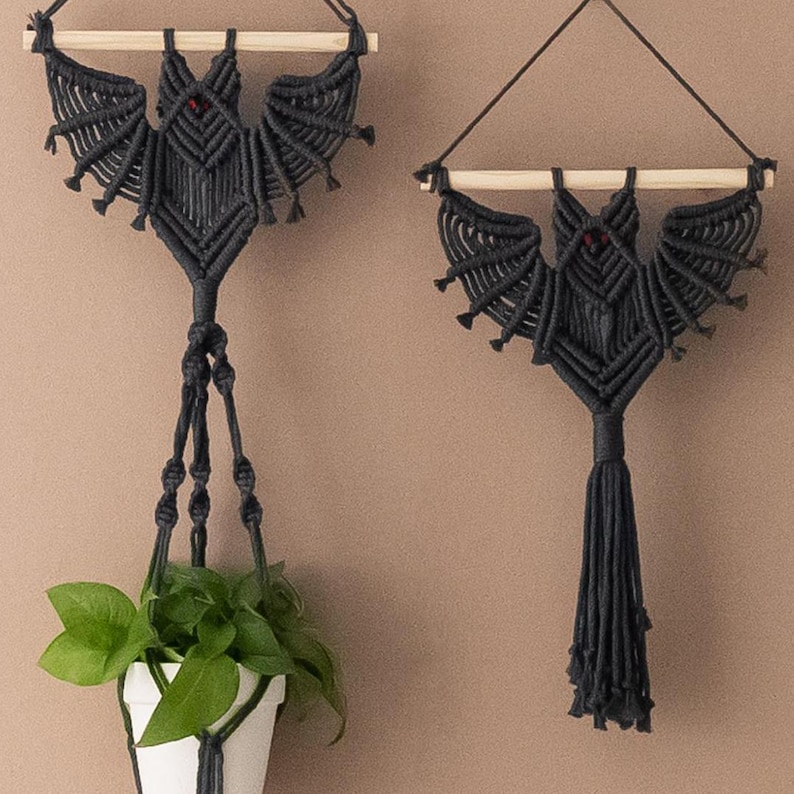 May include: Two black macrame bat wall hangings. One is a plant hanger with a wooden dowel and the other is a traditional wall hanging with a tassel.