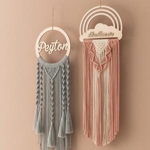 May include: Two wooden wall hangings with macrame details. The left one is a round hoop with the name "Peyton" written on it. The right one is a rainbow shape with a cloud that says "Kenzie".
