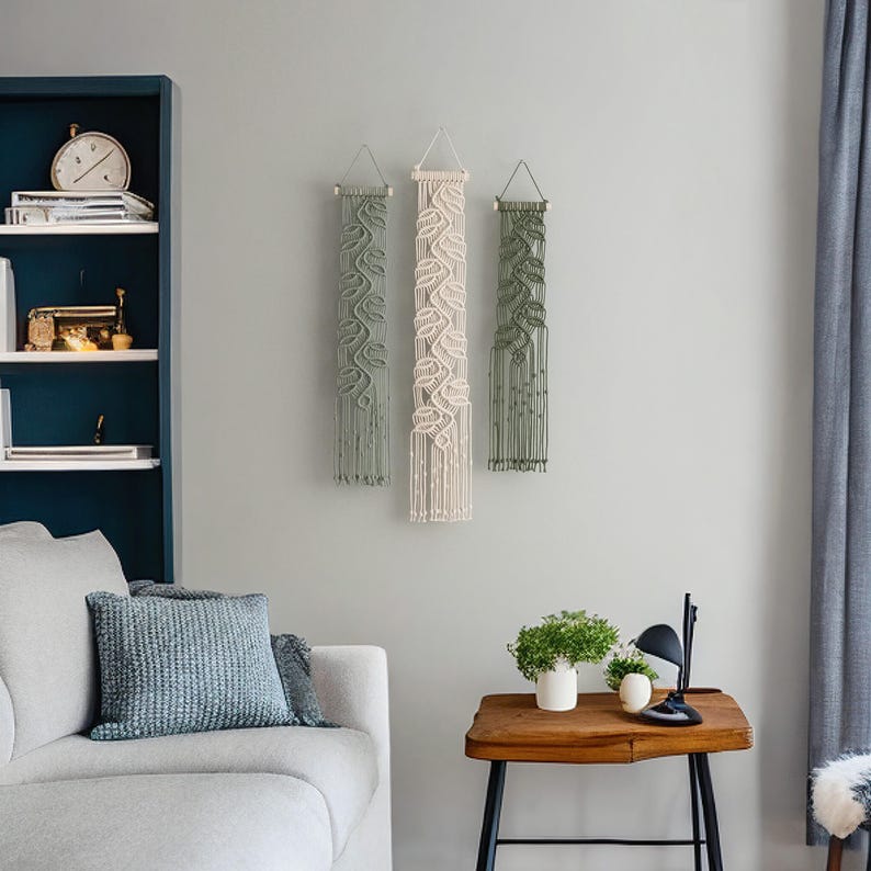 May include: Three macrame wall hangings with a leaf pattern. The hangings are in shades of green and cream. The hangings are displayed on a white wall in a living room setting.