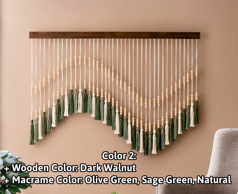 May include: A wall hanging made of macrame with wooden beads and tassels in olive green, sage green, and natural colors. The macrame is attached to a dark walnut wood bar.