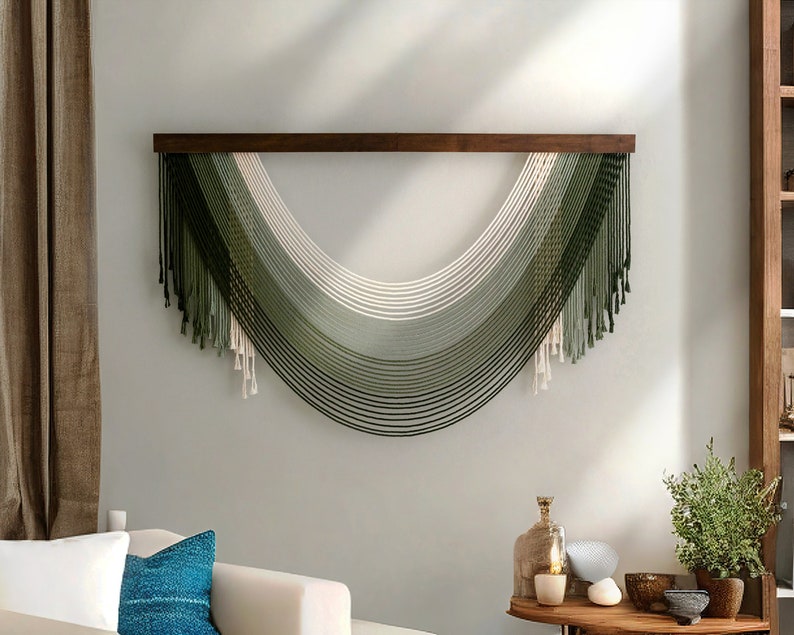 May include: A wall hanging made of woven yarn in shades of green and white. The yarn is arranged in a curved shape, creating a modern and minimalist design.