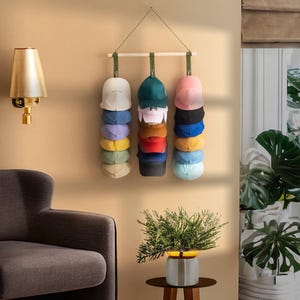 May include: A wall-mounted hat rack displaying a variety of baseball caps in different colors. The caps are stacked vertically, showcasing a range of hues from white and blue to red and black. The rack is suspended from a wooden bar.
