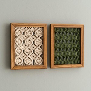 Pu&ograve; includere: Due arazzi da parete rettangolari in macram&egrave; in cornici di legno. Uno presenta un motivo intrecciato color crema, l'altro un design intrecciato verde. Le cornici sono di colore marrone chiaro e lo sfondo &egrave; grigio chiaro.