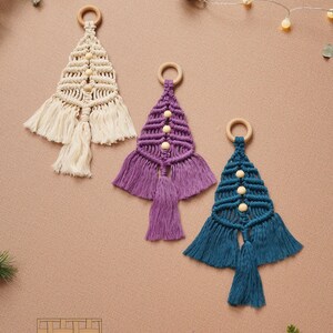 Puede incluir: Tres adornos de &aacute;rbol de Navidad de macram&eacute; hechos a mano con anillos de madera y cuentas. Los adornos son de color crema, morado y azul verdoso.