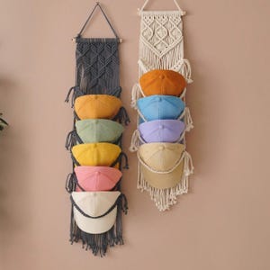 Peut inclure: Deux organisateurs muraux verticaux en macramé, l'un gris foncé et l'autre crème. L'organisateur gris foncé contient six casquettes de baseball en moutarde, vert sauge, jaune, rose et blanc. L'organisateur crème contient cinq casquettes orange, bleu, lavande et beige.