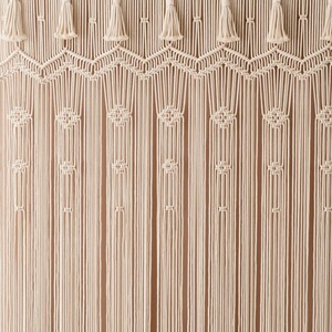 May include: A white macrame wall hanging with a geometric pattern and tassels. The hanging is made of cotton cord and has a natural, bohemian style.