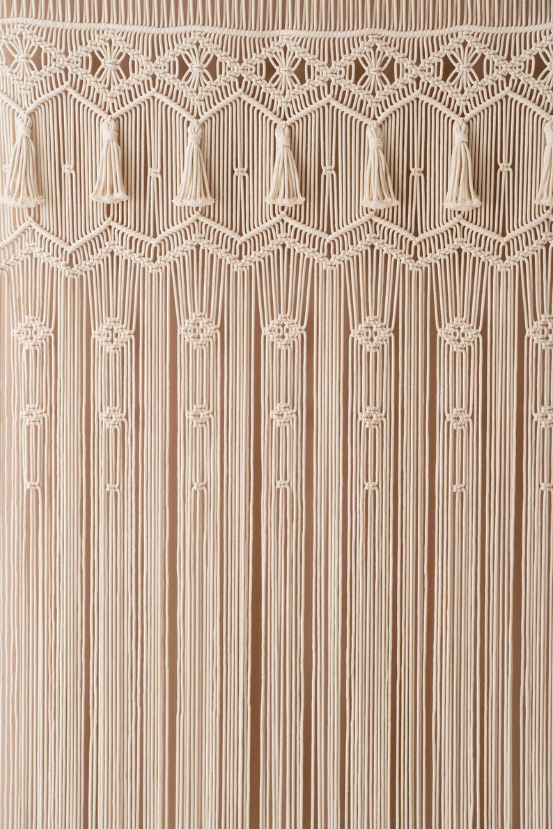 May include: A white macrame wall hanging with a geometric pattern and tassels. The hanging is made of cotton cord and has a natural, bohemian style.