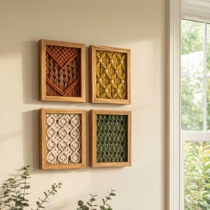 May include: Four framed macrame wall hangings in shades of orange, yellow, cream, and green. Each piece features a unique woven pattern within a natural wood frame. The artwork is displayed on a neutral wall, creating a warm, inviting aesthetic.