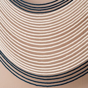 May include: A wall hanging made of white and dark blue rope, arranged in a curved pattern.