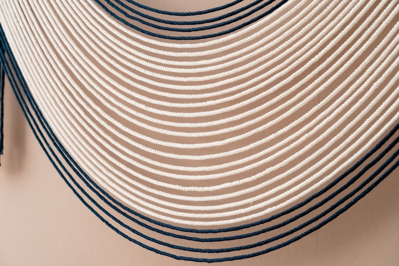 May include: A wall hanging made of white and dark blue rope, arranged in a curved pattern.