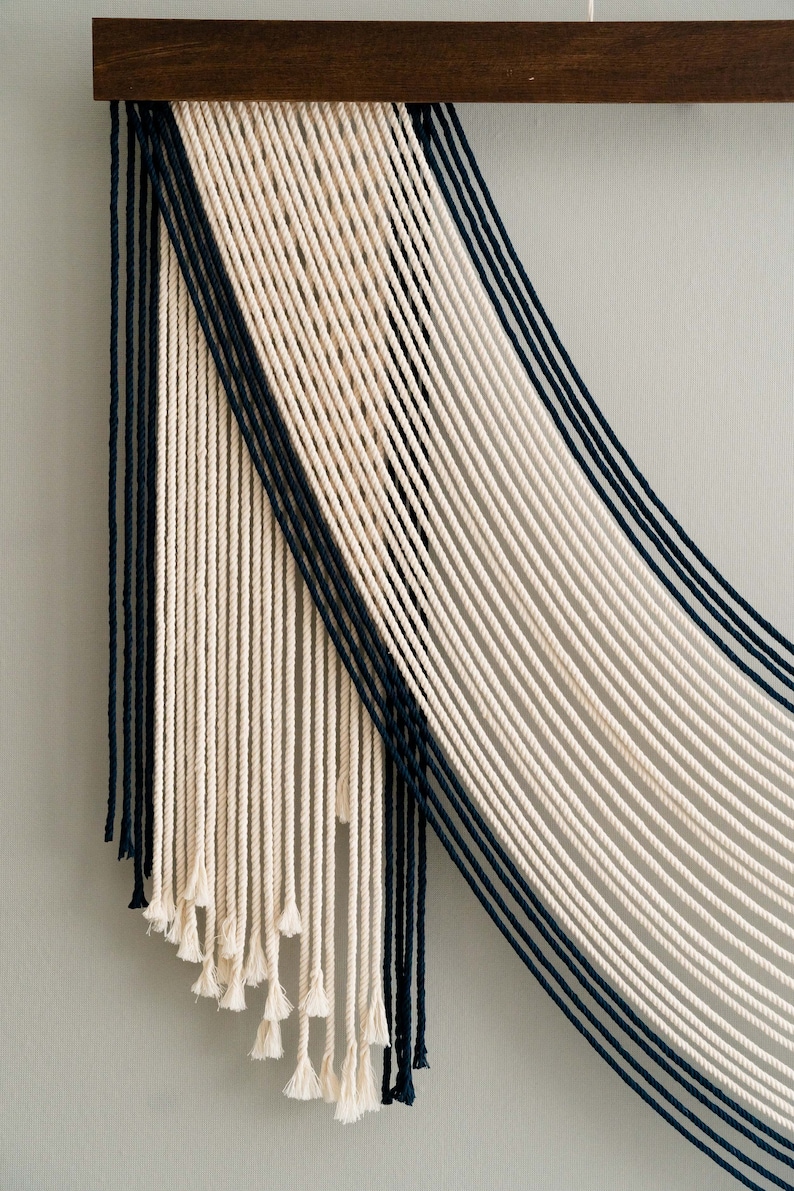 May include: A wall hanging made of white and black string, with a geometric pattern. The strings are woven together to create a modern and abstract design.