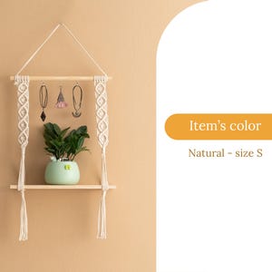 May include: A natural wood shelf with macrame hanging on each side. The shelf has a small potted plant on it and three earrings hanging from the macrame. The shelf is labelled "Item's colour: Natural - size S".