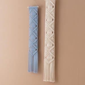 May include: Two macrame wall hangings with a diamond pattern. One is light blue and the other is cream.