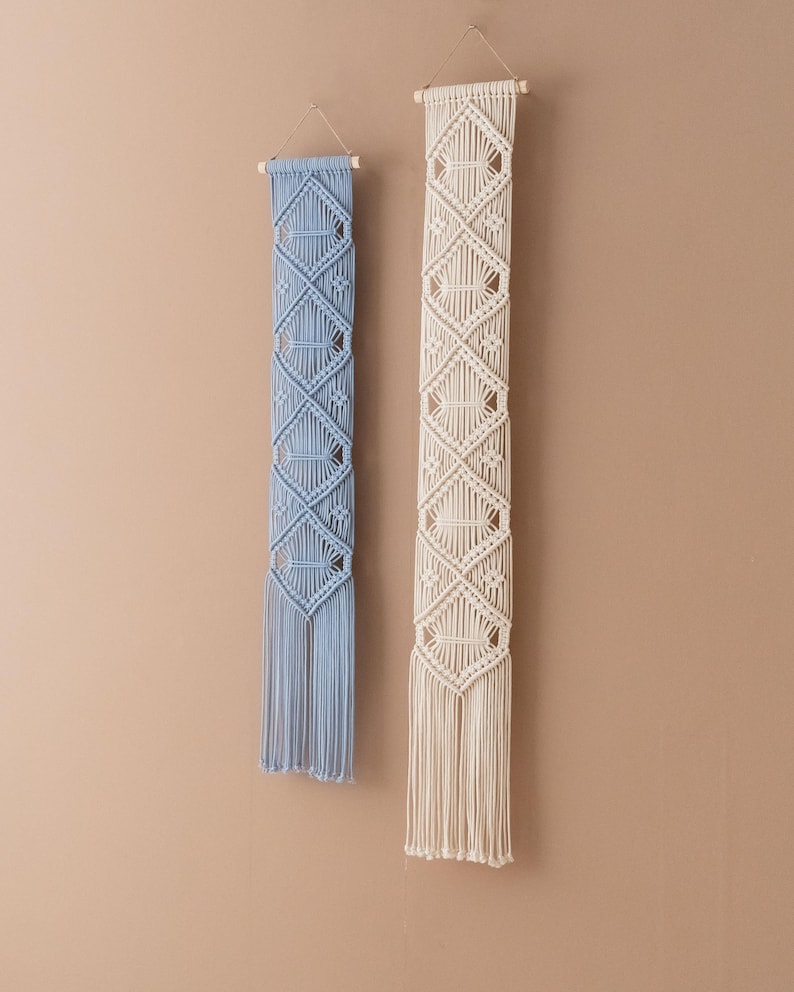 May include: Two macrame wall hangings with a diamond pattern. One is light blue and the other is cream.