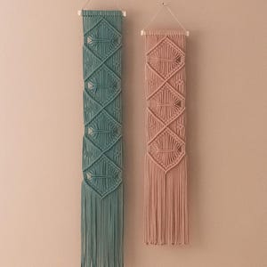 May include: Two macrame wall hangings, one in teal and one in dusty rose, with a diamond pattern and fringe.