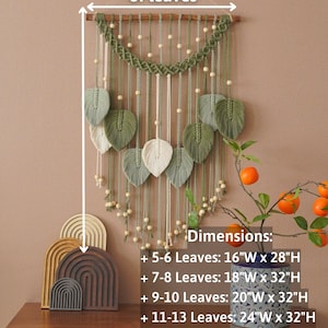 Op de afbeelding: Een macram&eacute; wandhanger met groene en witte bladeren, houten kralen en een houten lat aan de bovenkant. De wandhanger is 40,6 cm breed en 71,1 cm hoog wanneer deze 5-6 bladeren heeft. De afmetingen vari&euml;ren afhankelijk van het aantal bladeren.