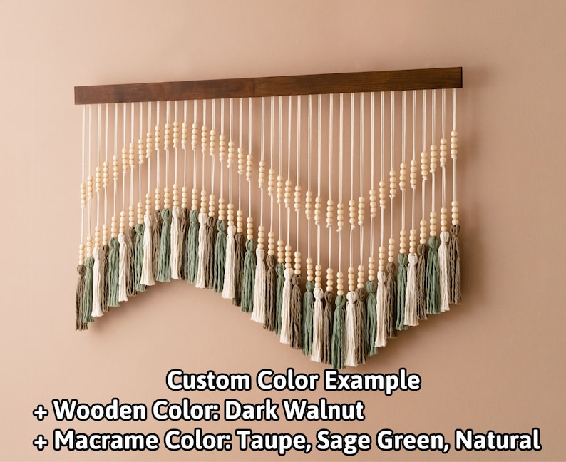 May include: A wall hanging with a wooden frame and a curved design made of white cord, wooden beads, and tassels in taupe, sage green, and natural colors. Custom Color Example + Wooden Color: Dark Walnut + Macrame Color: Taupe, Sage Green, Natural