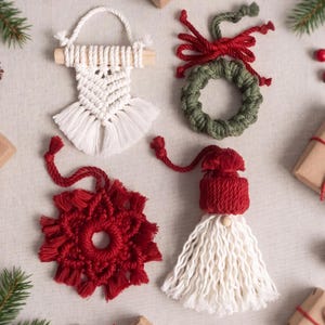 Puede incluir: Cuatro adornos de macramé hechos a mano que incluyen un tapiz blanco en un palo de madera, una corona verde con un lazo rojo, una pieza roja en forma de estrella y una figura de gnomo con gorro rojo y barba blanca de cordón anudado.