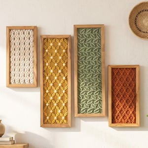 May include: Four rectangular wall art pieces in wooden frames featuring intricate macrame fiber art. The panels display cream, mustard yellow with wooden beads, sage green, and burnt orange knotted patterns in distinct geometric designs.