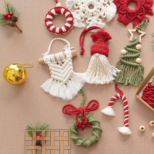 May include: A collection of handmade Christmas ornaments made with macrame. The ornaments include a snowflake, a wreath, a candy cane, a gnome, a Christmas tree, and a circle with red and white stripes. The ornaments are all made with natural fibers and have a rustic, handmade look.