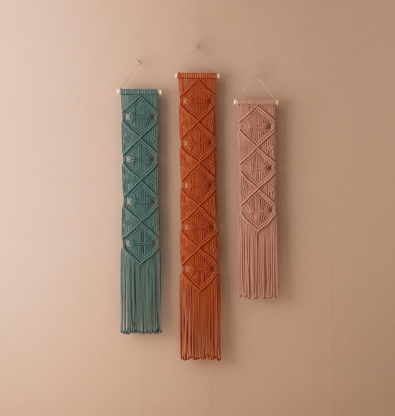 May include: Three macrame wall hangings with geometric patterns. The hangings are in shades of teal, orange, and pink.