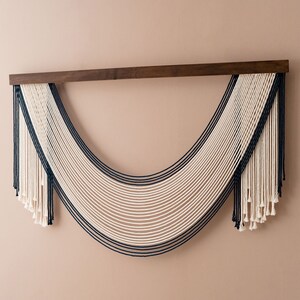 May include: A wall hanging made of white and dark blue yarn, with a wooden dowel at the top. The yarn is woven into a curved shape, creating a modern and minimalist design.