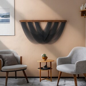 May include: A wall hanging featuring a horizontal wooden bar with multiple dark gray cord strands draped in a series of overlapping, U-shaped curves. The cords are suspended from the wood, creating a layered, fan-like pattern across the wall.