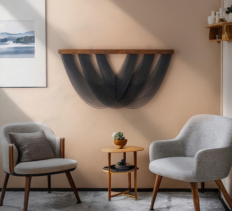 May include: A wall hanging featuring a horizontal wooden bar with multiple dark gray cord strands draped in a series of overlapping, U-shaped curves. The cords are suspended from the wood, creating a layered, fan-like pattern across the wall.