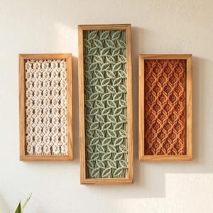 May include: Three rectangular wooden frames containing macrame wall art. The left frame features cream-colored knotted cord, the center taller frame displays sage green leaf-patterned macrame, and the right frame shows rust-colored diamond-patterned cord.