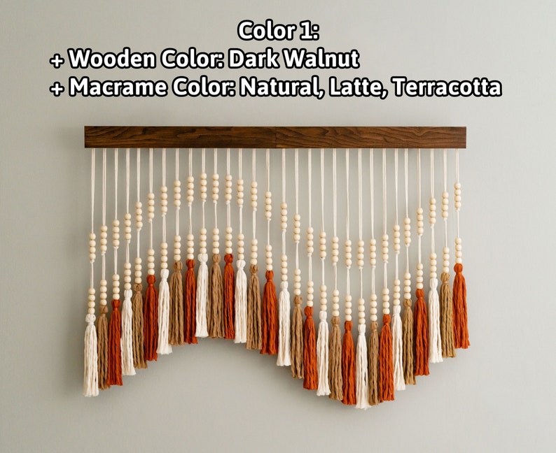May include: A wall hanging with a dark walnut wood bar and white and natural colored macrame with terracotta, latte, and natural colored tassels.
