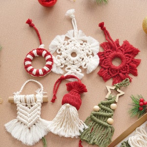 May include: Six handmade Christmas ornaments made of macrame with various designs, including a snowflake, a star, a tree, a wreath, a gnome, and a flower. The ornaments are made with white, red, and green yarn.