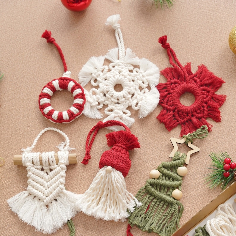May include: Six handmade Christmas ornaments made of macrame with various designs, including a snowflake, a star, a tree, a wreath, a gnome, and a flower. The ornaments are made with white, red, and green yarn.