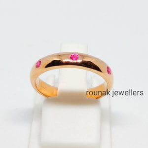 May include: A gold band ring with four small pink gemstones set into the band. The ring is on a white display stand.  rounak jewellers